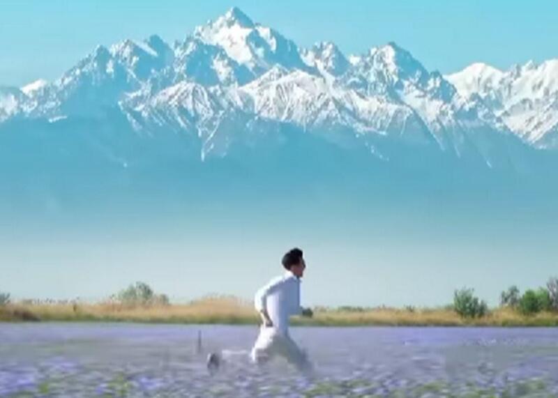 A man runs through a purple flower field with snow-capped mountains in the background under a clear blue sky.