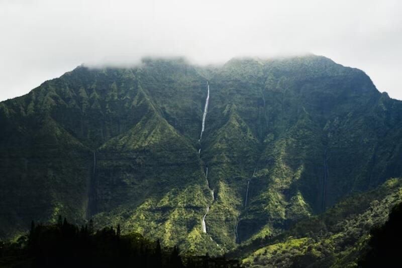 A mountain with green vegetation is partially covered in fog, and several waterfalls cascade down its slopes.