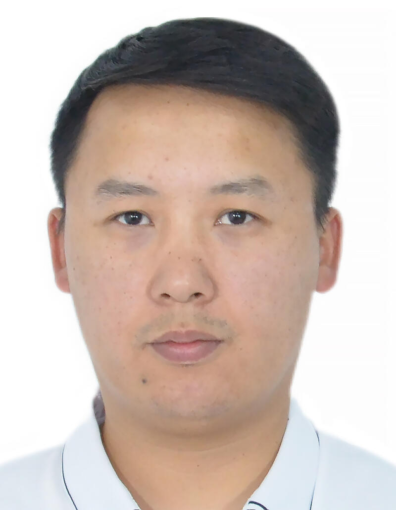 A portrait of a man with short black hair, light skin, and a mole on his face, wearing a light blue collared shirt.