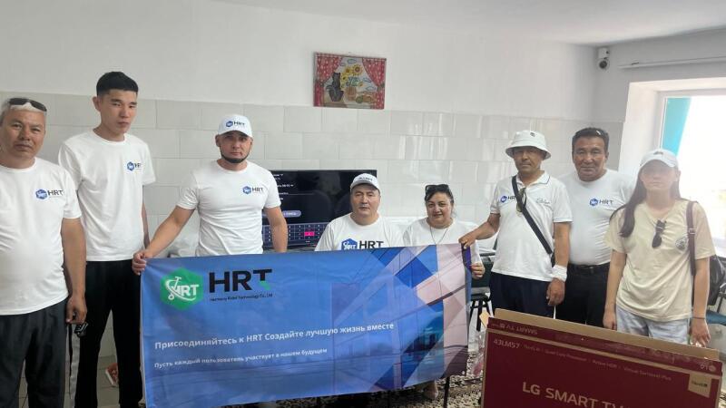 Группа людей держит баннер HRT с надписью «Присоединяйтесь к HRT Создайте лучшую жизнь вместе» и коробку для телевизора LG Smart TV.