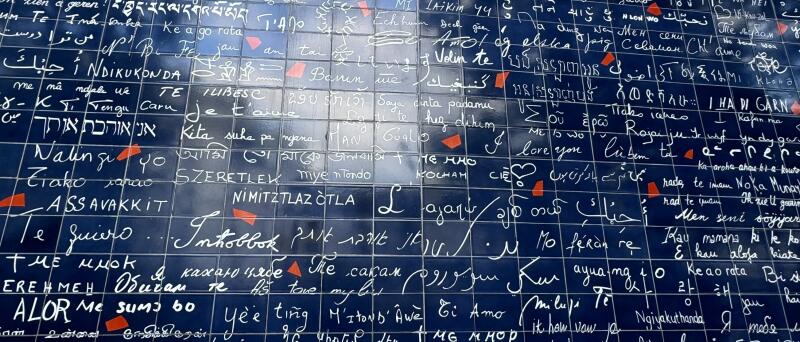 A wall of dark blue tiles covered in the phrase 'I love you' in many different languages and scripts, with small red squares scattered throughout.