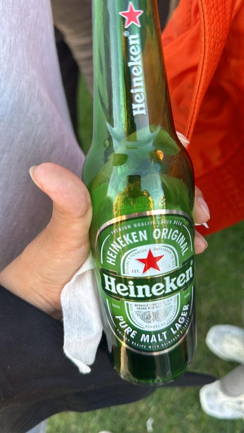 Человек держит зеленую бутылку пива Heineken с красной звездой на этикетке.