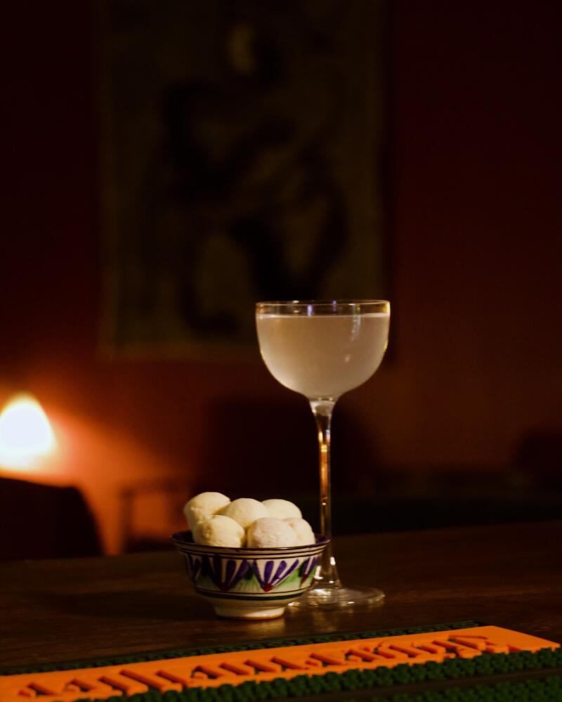 A stemmed glass of clear liquid sits next to a small bowl filled with white balls, on a dark wooden surface.