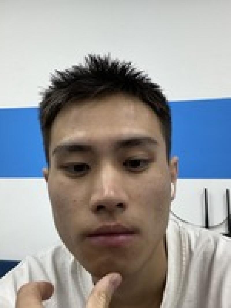 A close-up of a person with dark hair is shown with their hand touching their chin, with a white and blue wall in the background.