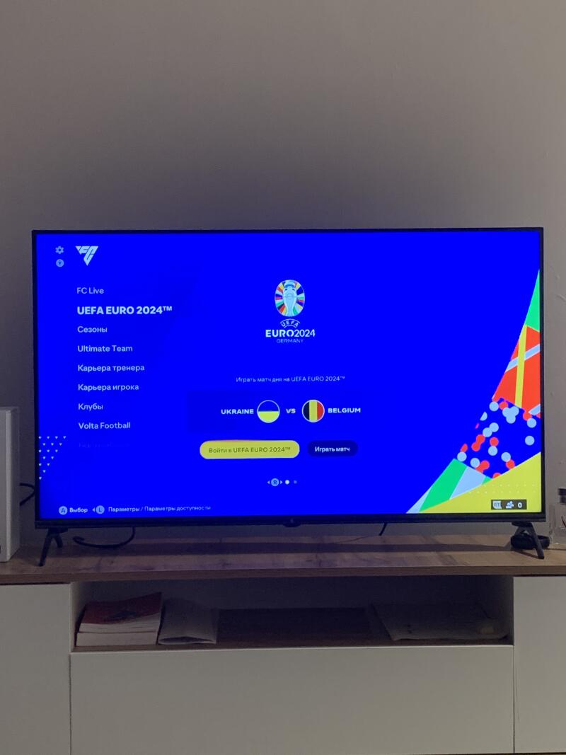 A TV displaying the UEFA EURO 2024 game menu, featuring options like Seasons, Ultimate Team, and Volta Football, with Ukraine versus Belgium highlighted as a match.