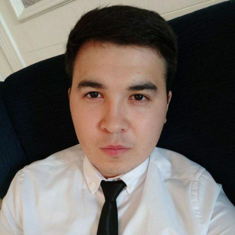 A man with dark hair is wearing a white shirt and a black tie.