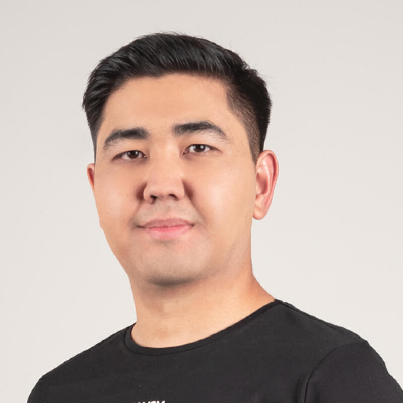 A portrait of a man with dark hair wearing a black T-shirt against a light background.