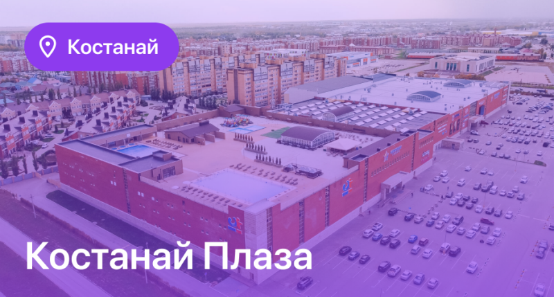 An aerial shot of Kostanay Plaza, a large shopping mall with a full parking lot, with "Kostanay" in a purple pin and the mall name at the bottom.