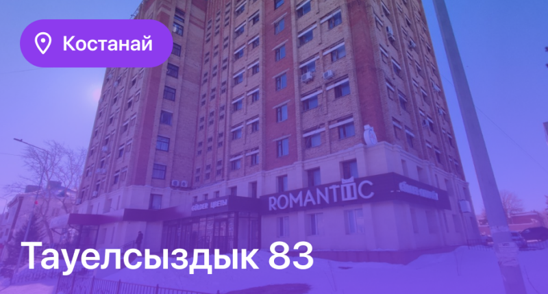 The image shows a tall brick building with many windows, under a blue sky. Text on the image reads 'Костанай' and 'Тәуелсіздік 83'.