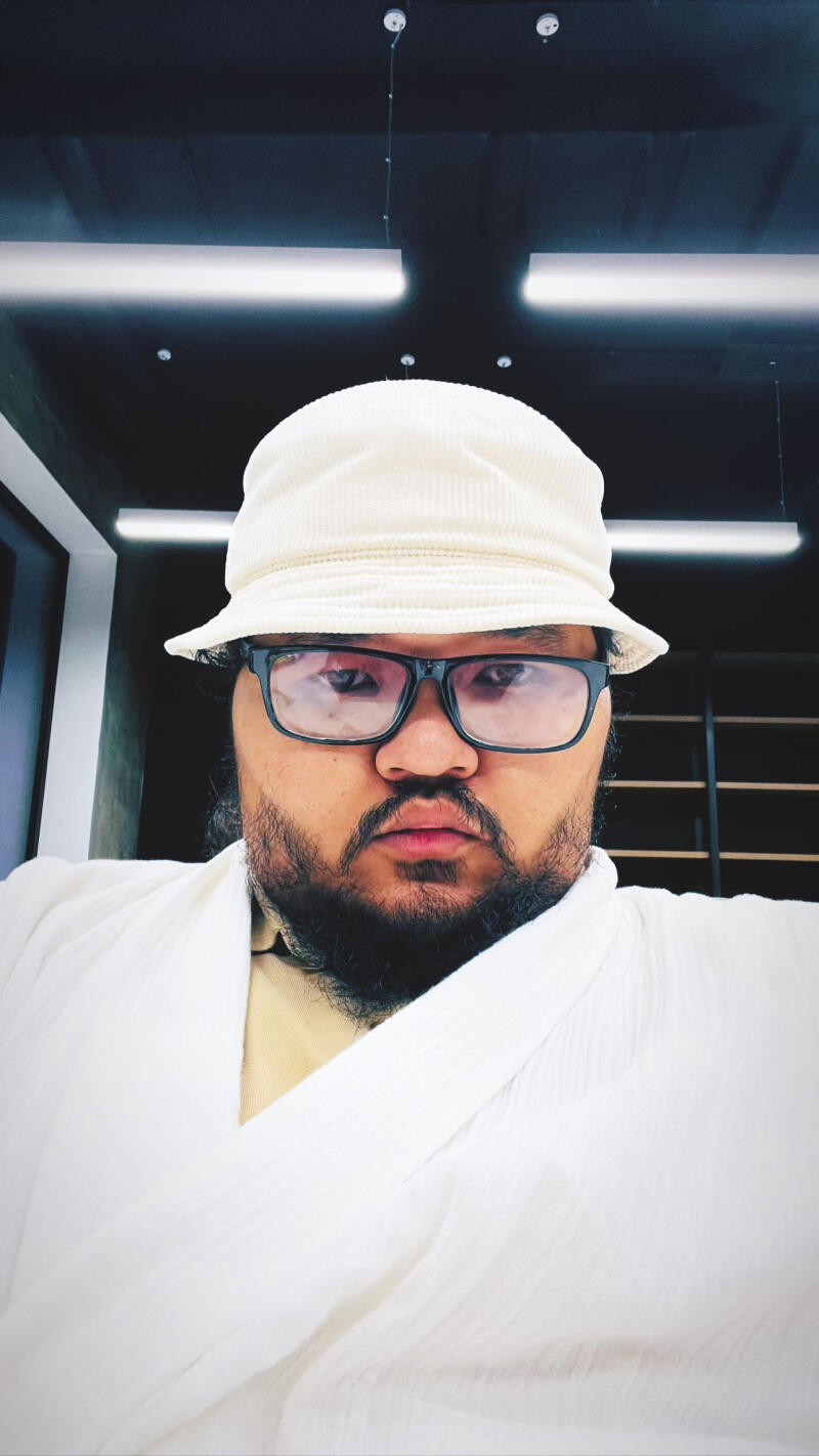 A man with glasses and a beard is wearing a white bucket hat and a white robe.