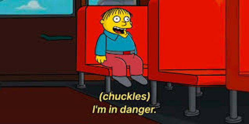 Ralph Wiggum is sitting on a red bus seat and says, "(chuckles) I'm in danger."