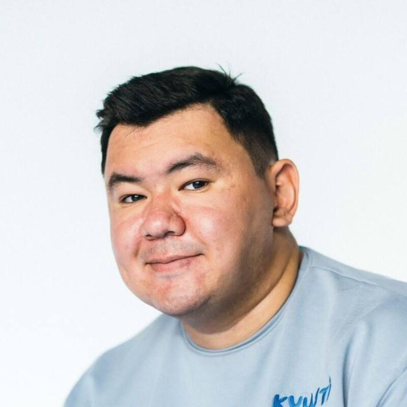 A portrait of a man with short dark hair and a light blue shirt. The shirt has the word 'KYZYL' written in blue letters.