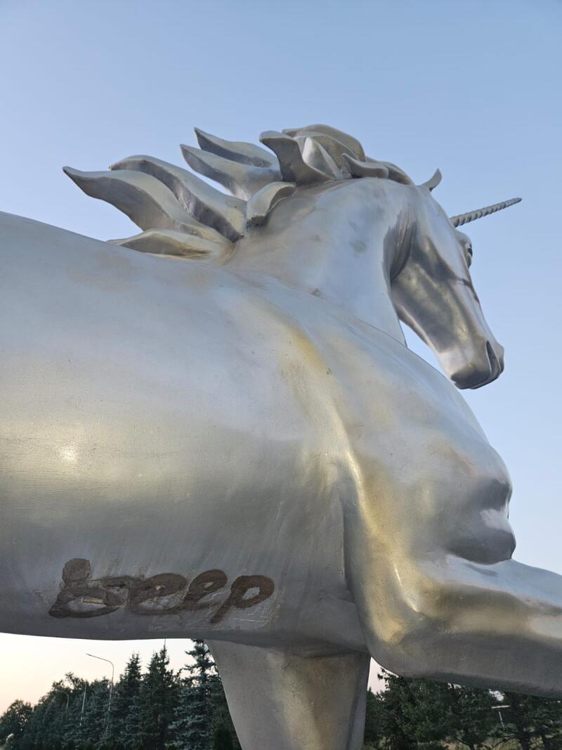 A low-angle shot of a silver unicorn statue against a blue sky, with the word "beep" written on its side.
