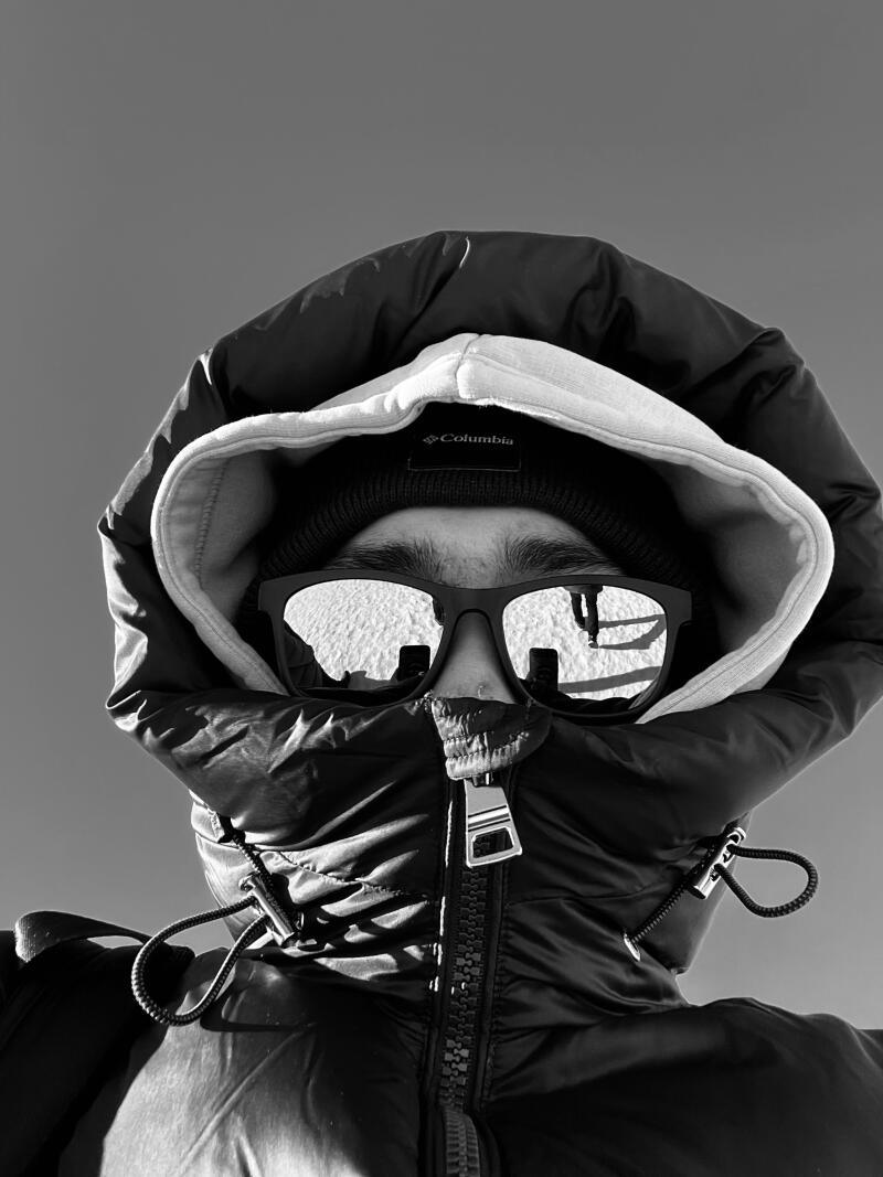 A monochrome close-up shows a person wearing sunglasses and a hooded jacket, with a 'Columbia' logo visible on their hat; the sunglasses reflect a snowy landscape with a figure standing in it.