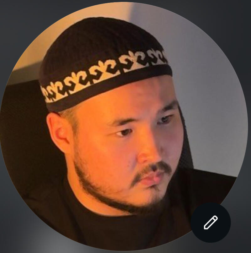 A portrait of a man with a beard wearing a black taqiyah with a white pattern, set against a blurred background.