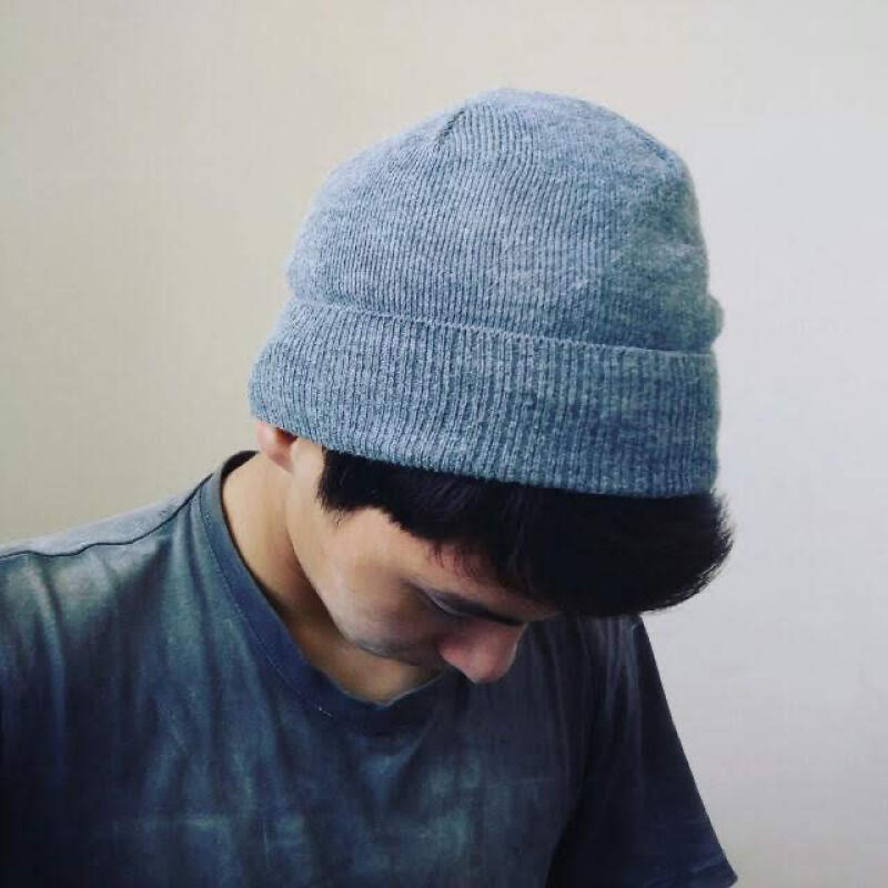 A person is wearing a gray beanie and a gray t-shirt, looking down with their head slightly bowed.