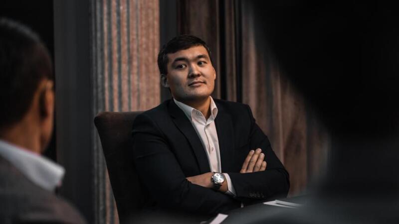 A man in a suit and dress shirt sits with his arms crossed, wearing a watch.