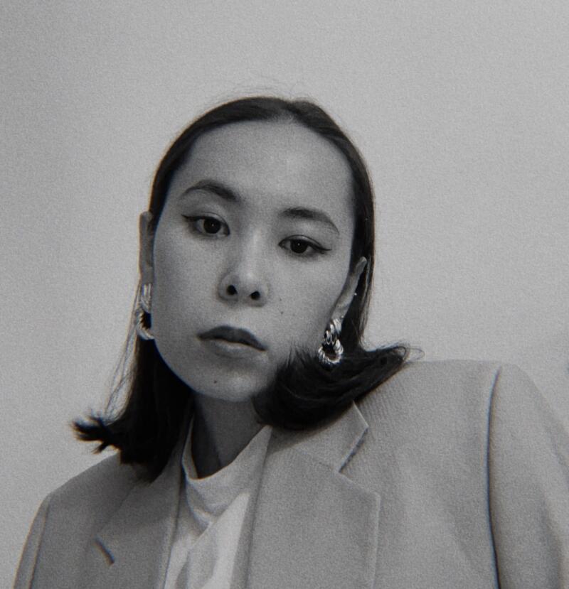 A grayscale portrait of a woman with short, dark hair wearing a light-colored blazer and hoop earrings.