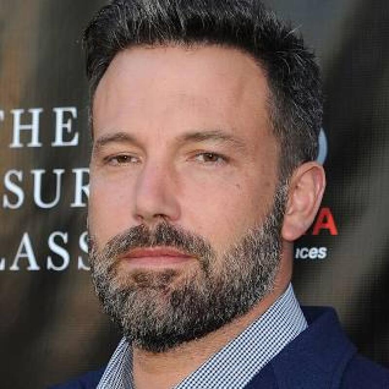 A medium shot shows a man with short graying hair and a beard wearing a blue and white checkered shirt and a blue jacket.