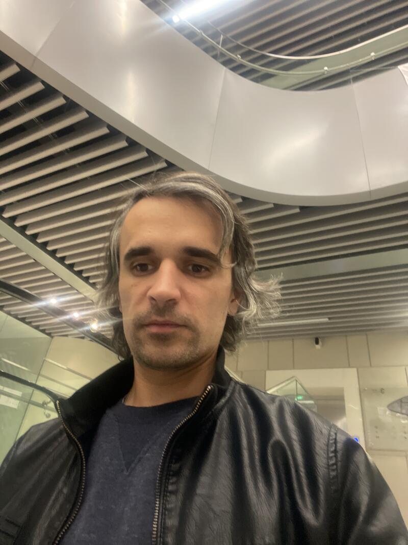 A man with graying hair and a black leather jacket stands beneath a modern, slatted ceiling.