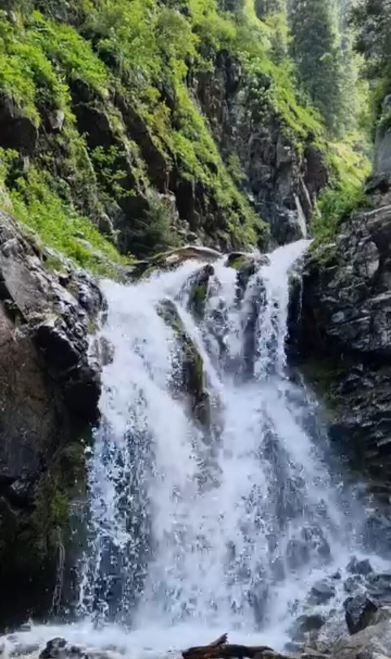 A waterfall cascades down a rocky slope covered with green vegetation.