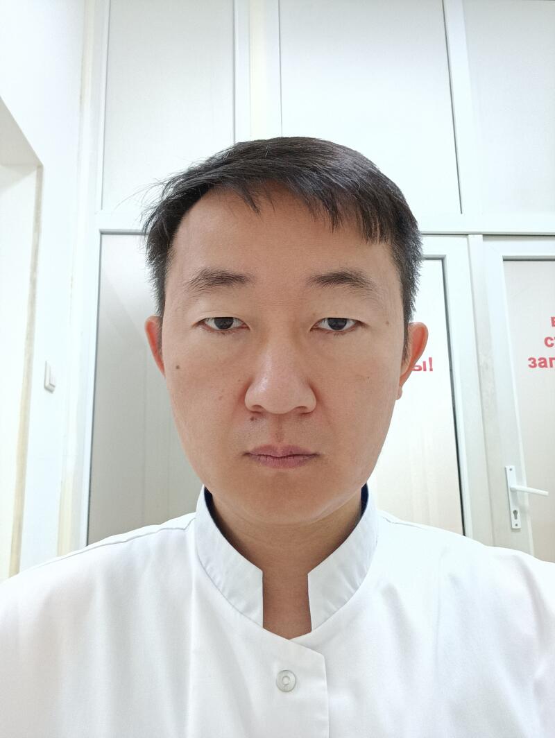 A portrait of an Asian man with short dark hair, wearing a white coat, against a white door background.