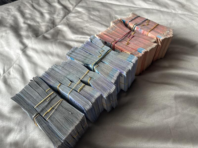 The image shows stacks of banded currency arranged diagonally on a gray fabric surface.