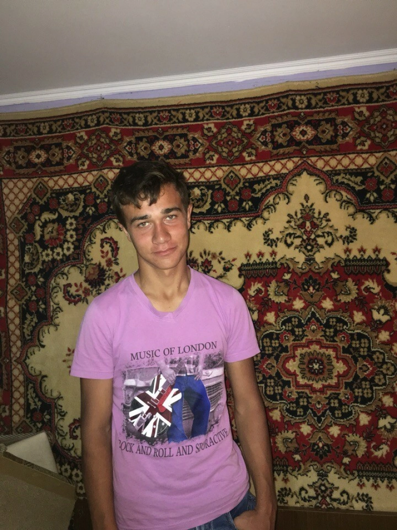 A young man in a lilac T-shirt with the inscription "MUSIC OF LONDON ROCK AND ROLL AND SPURACTIVE" stands against the background of a patterned carpet.