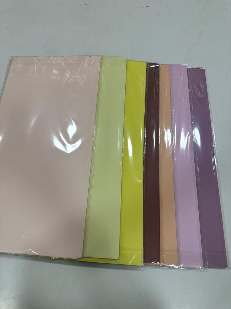 The image shows a stack of colorful paper sheets, individually wrapped in transparent plastic, arranged side by side.