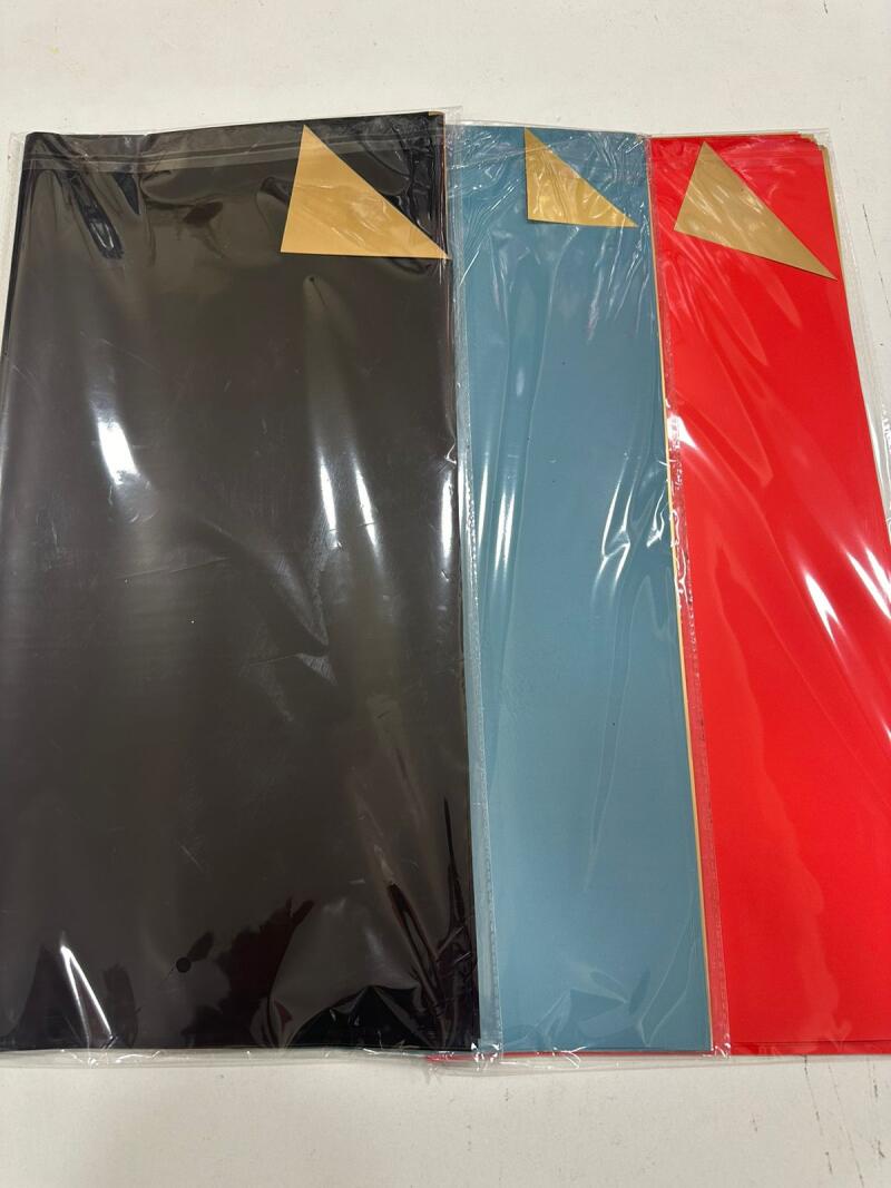 Three sheets of colored paper, black, blue, and red, are each individually wrapped in clear plastic.