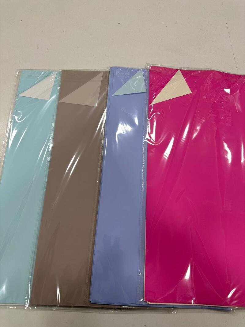 The image shows four stacks of colored paper in plastic sleeves: light blue, brown, blue, and pink.