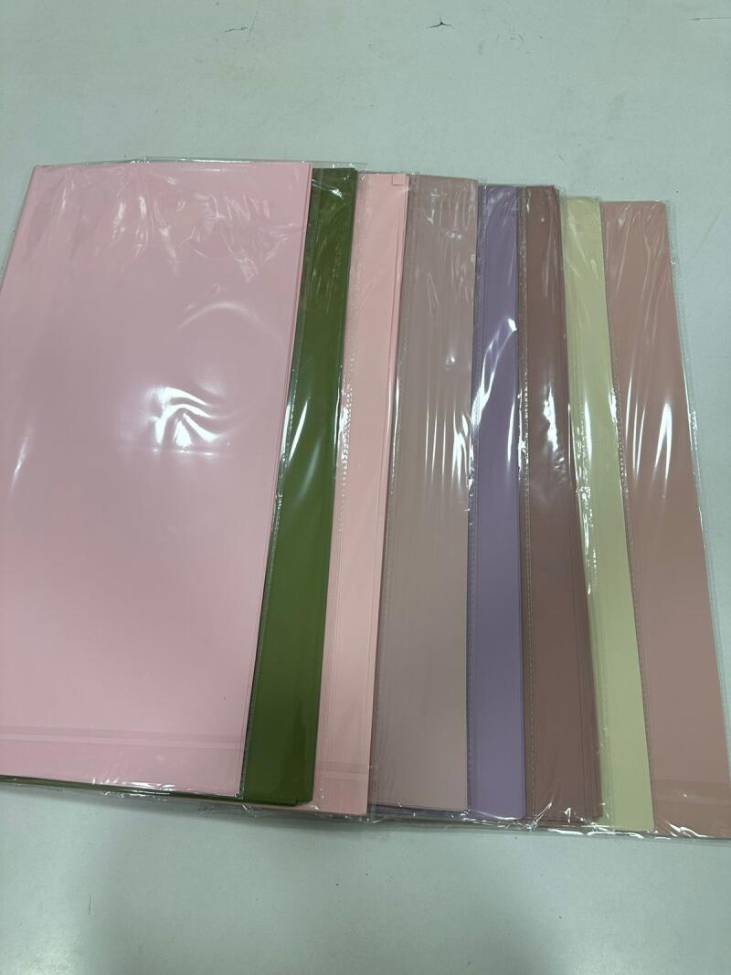 A row of colorful folders are arranged neatly, featuring shades of pink, olive green, lavender, and beige, all appearing to be wrapped in clear plastic.