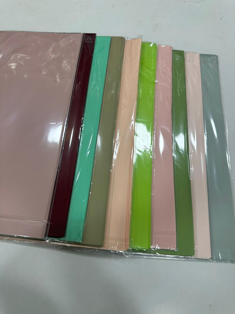 A stack of colored papers is arranged in a row, each wrapped in clear plastic sleeves.
