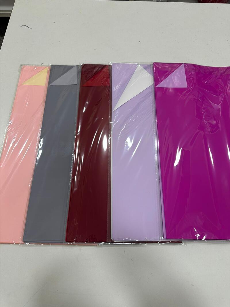 The image shows several sheets of colored paper, individually wrapped in clear plastic, arranged in a row on a white surface. The colors of the paper range from light pink to dark purple.