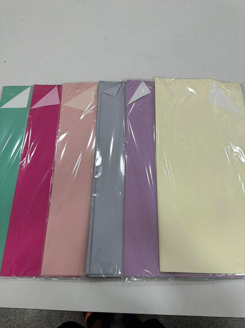 The image shows a set of colorful papers, wrapped in a transparent plastic film, lined up on a white table.