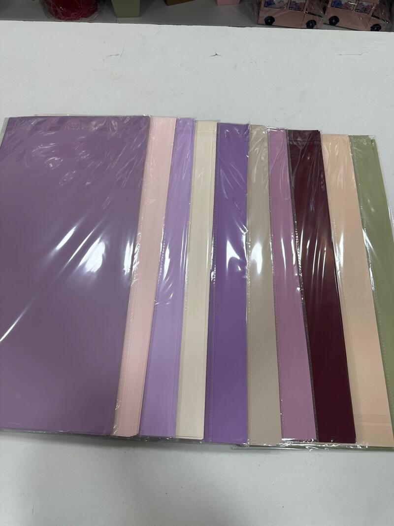 The image shows a row of colorful paper stacks, each wrapped in plastic, with colors including purple, pink, beige, burgundy, and green.