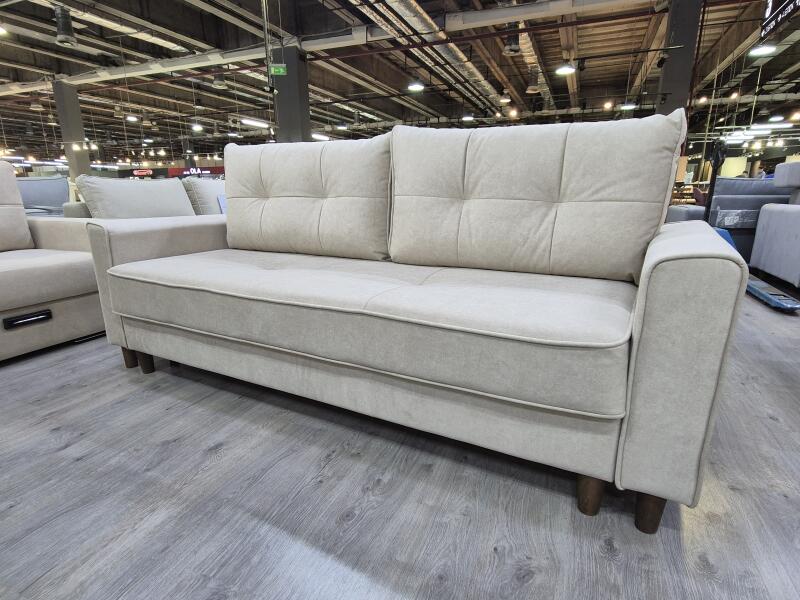 A beige sofa with square-patterned cushions sits on a gray wood floor in a furniture store.