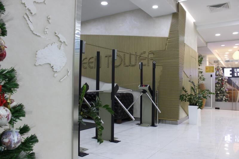 The image shows an office interior with a turnstile entrance, a textured wall with a world map, and a Christmas tree in the background.