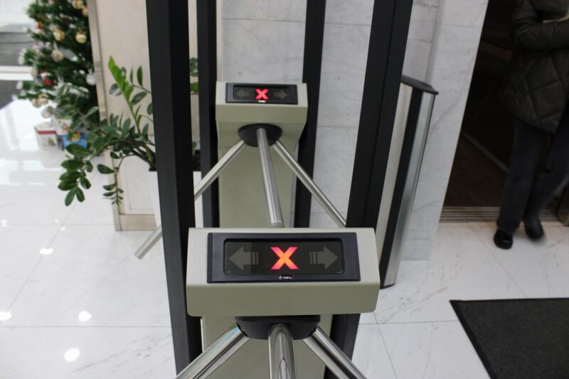 A turnstile with a red X displayed, indicating access is denied, is positioned in front of a person walking through a doorway.