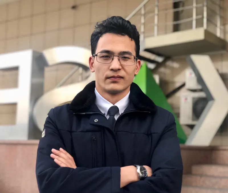 A man in glasses and a jacket with his arms crossed stands in front of a building with the letters KASE.