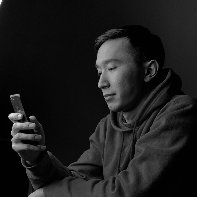 A person in a hoodie is looking at a cell phone in their hand in a black and white photo.