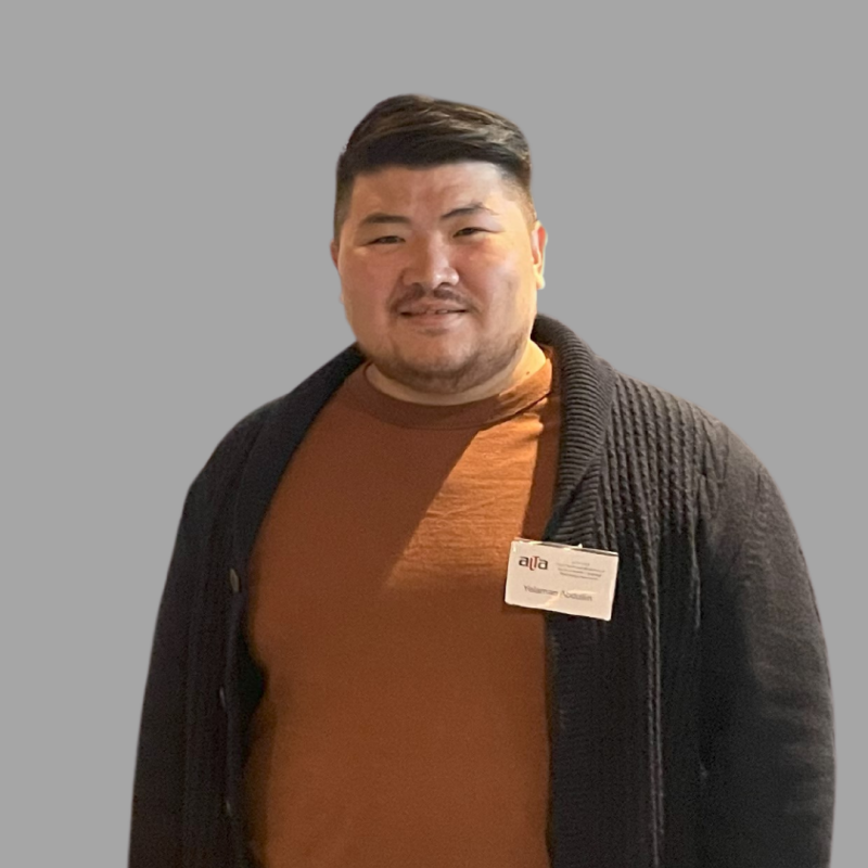 A man is wearing a brown shirt and a black cardigan, with a name tag that reads "affa Volkaner Asmalian."