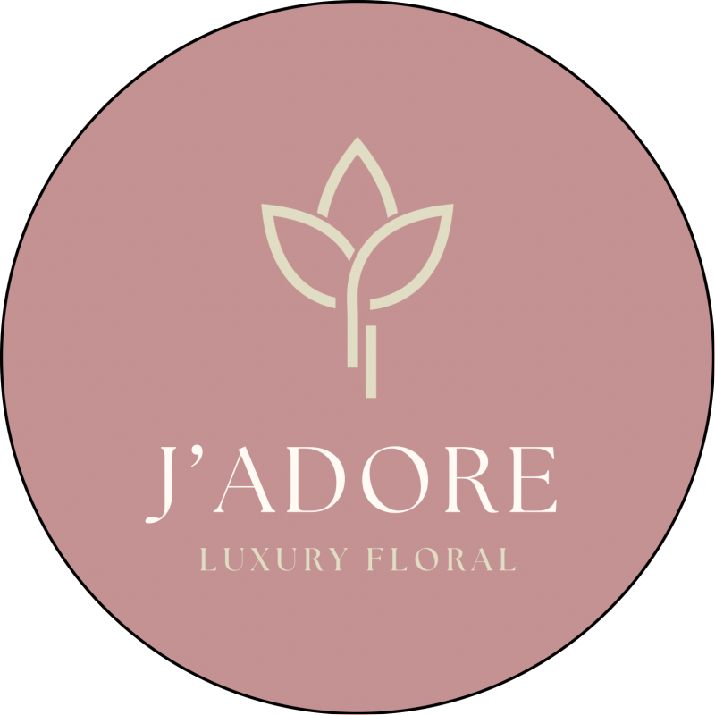 The image is a round logo on a pink background with a floral design and the text "J'ADORE LUXURY FLORAL" in light beige color.