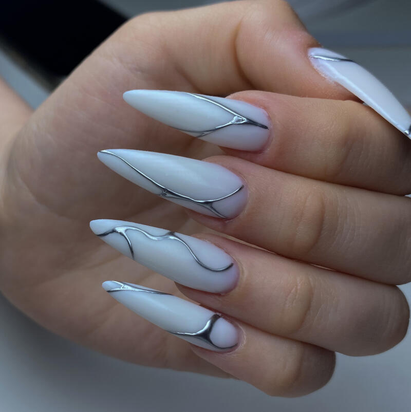 A close-up shot shows a hand with stiletto-shaped nails, each painted white and adorned with abstract silver lines that curve and flow across the surface.