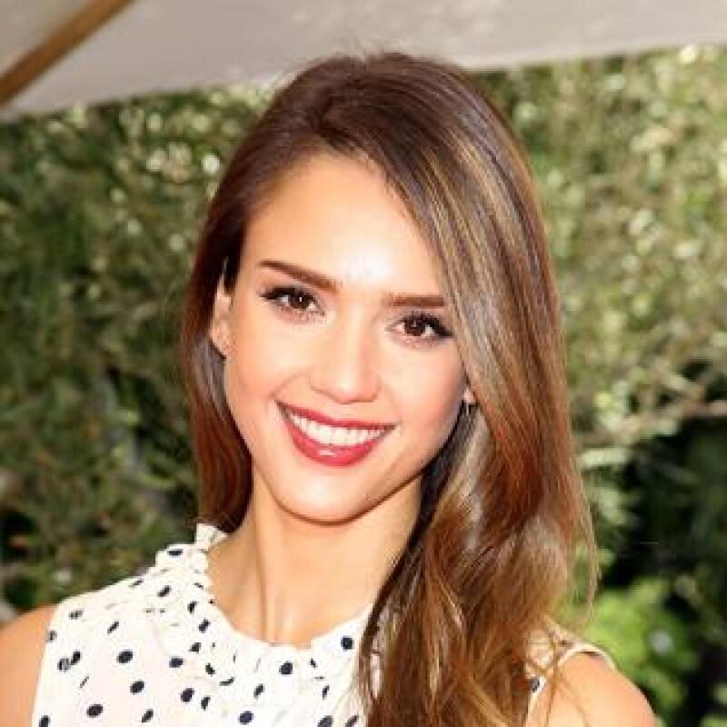 A smiling woman with long brown hair and red lipstick is wearing a white and black polka dot top.