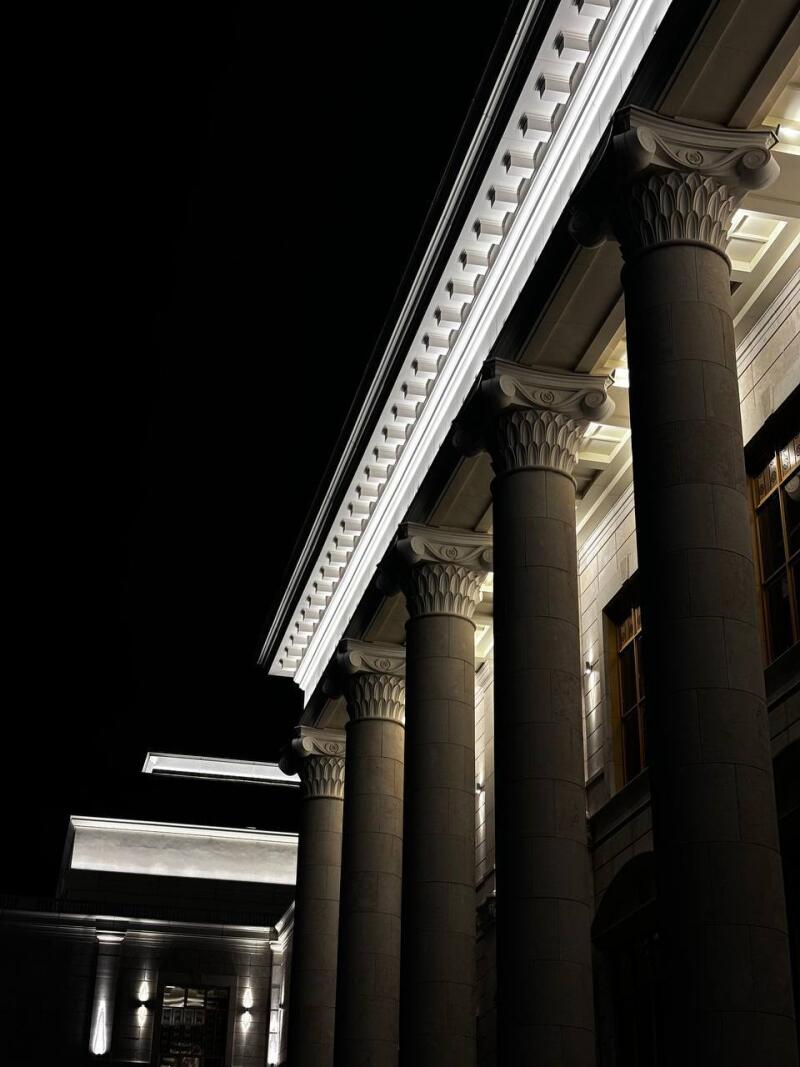 A low-angle shot captures illuminated architectural columns against a dark sky, featuring ornate capitals and detailed entablature.
