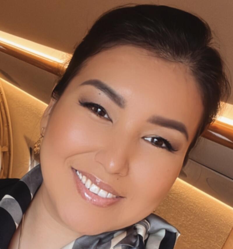 A close-up of a woman with brown hair, smiling and wearing a black and white patterned scarf.
