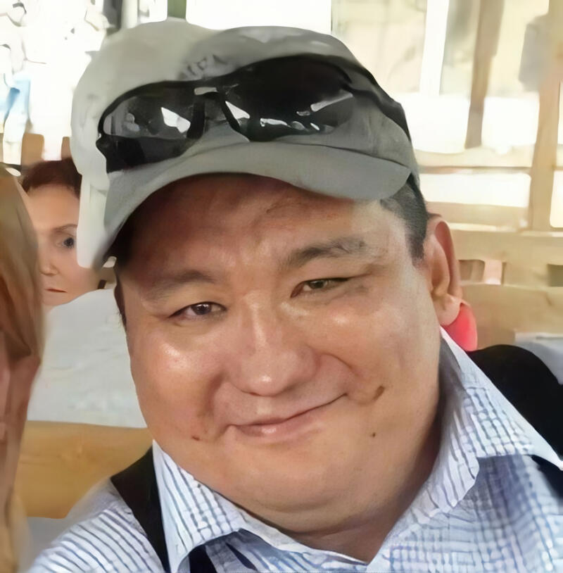 A smiling man wearing a cap and sunglasses is pictured in a close-up shot.