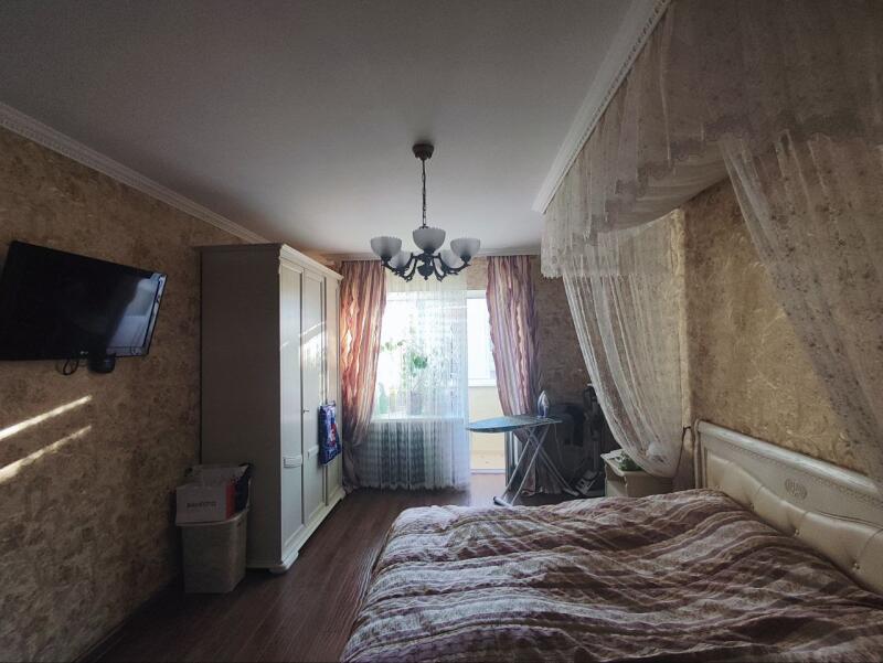 The bedroom features a bed with patterned bedding, a wardrobe, a TV on the wall, and a balcony with curtains.
