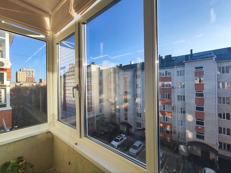 From a balcony, a view is seen through windows of buildings, cars, and a blue sky.
